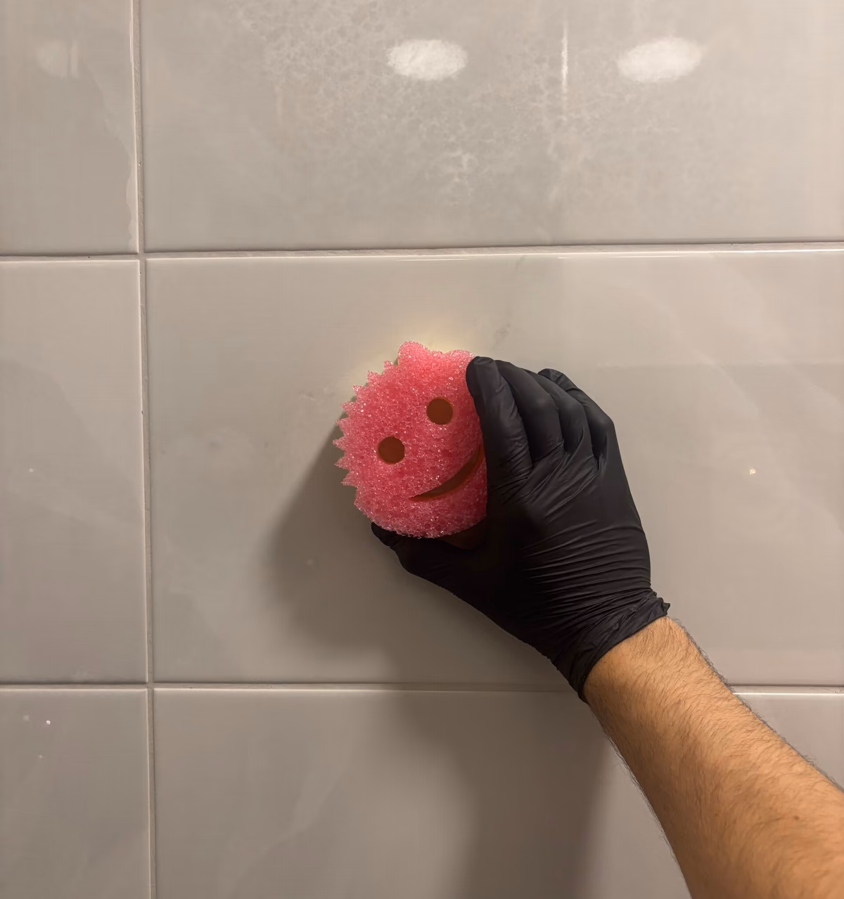 Kiiltävän laattaseinän puhdistus pesusienellä, suojakäsine kädessä